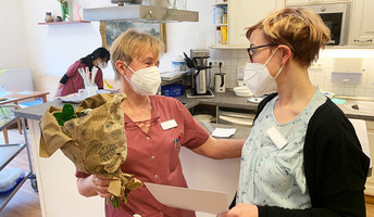 Einrichtungsleiterin gratuliert Mitarbeiterin und überreicht Blumenstrauß