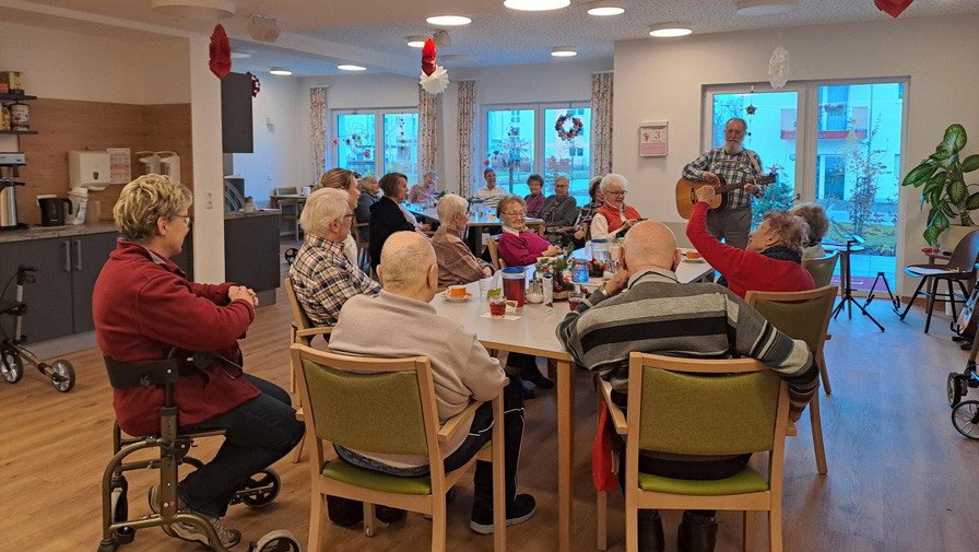 Bei der Adventsparty in der ProCurand Tagespflege Strausberg genießen die Tagesgäste die festliche Stimmung, während Musiker Klaus Schluchter mit Gitarre und Mundharmonika für musikalische Unterhaltung sorgt