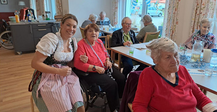 Eine Mitarbeiterin in Dirndl hat viel Spaß mit den Bewohner*innen während des Oktoberfests in der ProCurand Tagespflege Strausberg und sorgt für ausgelassene Stimmung.