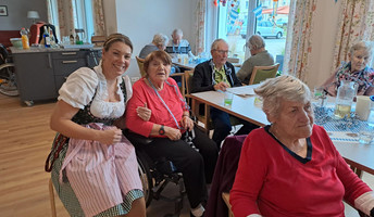 Eine Mitarbeiterin in Dirndl hat viel Spaß mit den Bewohner*innen während des Oktoberfests in der ProCurand Tagespflege Strausberg und sorgt für ausgelassene Stimmung.