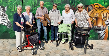 Mieter*innen der ProCurand Seniorenresidenz Am Straussee posieren vor der Wand des Parks, die mit lebendigem Tiergraffiti geschmückt ist, und genießen ihren Ausflug in Willes Welt.