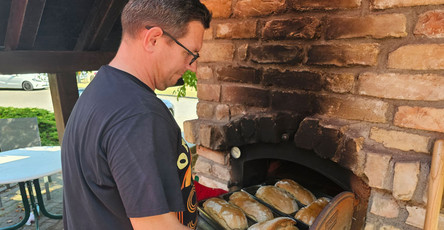 Ein Mitarbeiter der ProCurand Seniorenresidenz Am Görnsee schiebt köstliche Sandwiches in den Steinofen während des traditionellen Backofenfests.