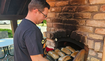 Ein Mitarbeiter der ProCurand Seniorenresidenz Am Görnsee schiebt köstliche Sandwiches in den Steinofen während des traditionellen Backofenfests.