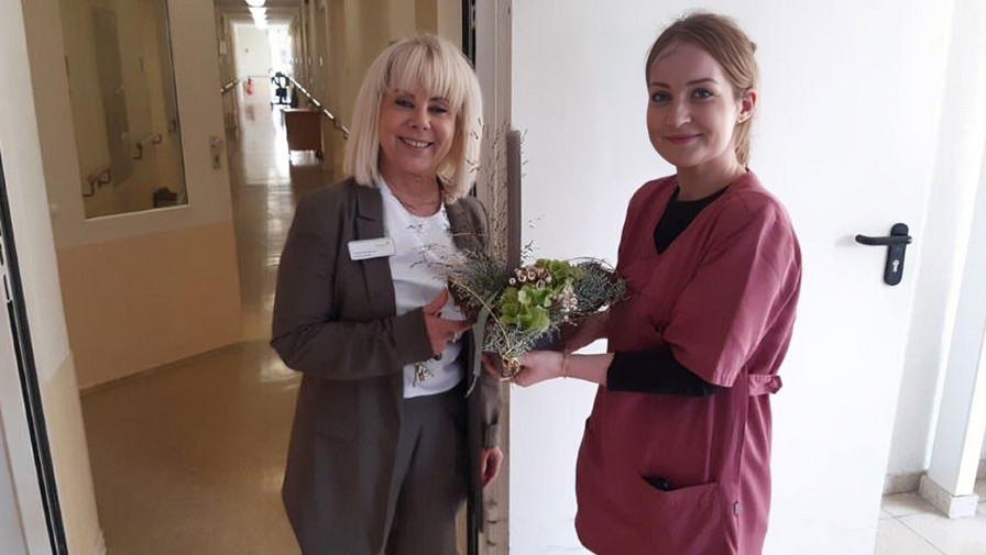 Francie Brähmig, die erste erfolgreiche Absolventin des APH-Kurses in der ProCurand Seniorenresidenz Sanft am See, erhält stolz einen Blumenstrauß zur Feier ihres bestandenen Kurses. 