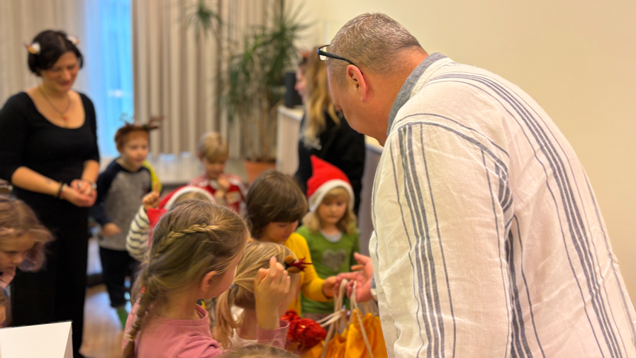 Einrichtungsleiter Matthias Küßner übergibt den fröhlichen Kita-Kindern in der ProCurand Seniorenresidenz Bölschestraße als Dankeschön bunte Bälle und süße Naschereien.