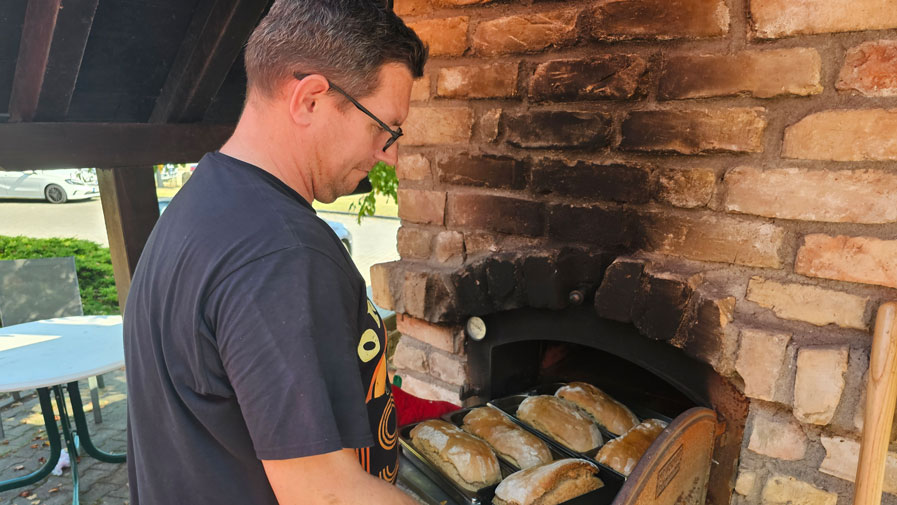 Ein Mitarbeiter der ProCurand Seniorenresidenz Am Görnsee schiebt köstliche Sandwiches in den Steinofen während des traditionellen Backofenfests.