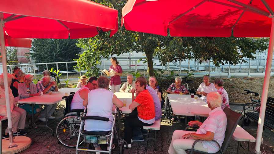 Viele Bewohner*innen der ProCurand Seniorenresidenz Am Görnsee sitzen entspannt an Tischen draußen und warten voller Vorfreude auf die leckeren Speisen des Backofenfests. Die Stimmung ist fröhlich und gesellig!